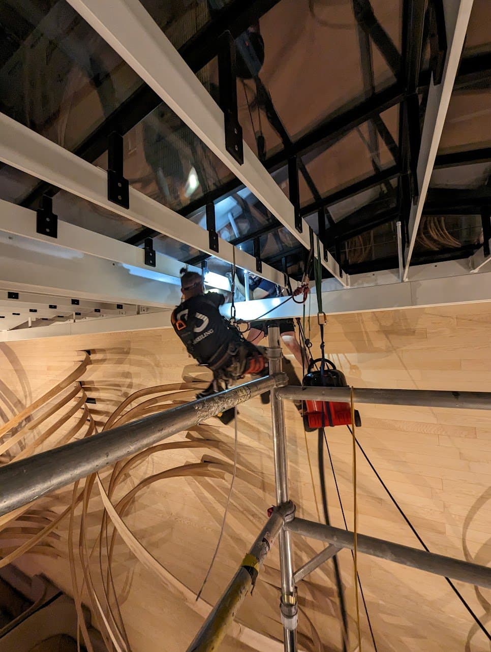 Technician suspended from the atrium beams working above an aluminium tower on the lobby floor