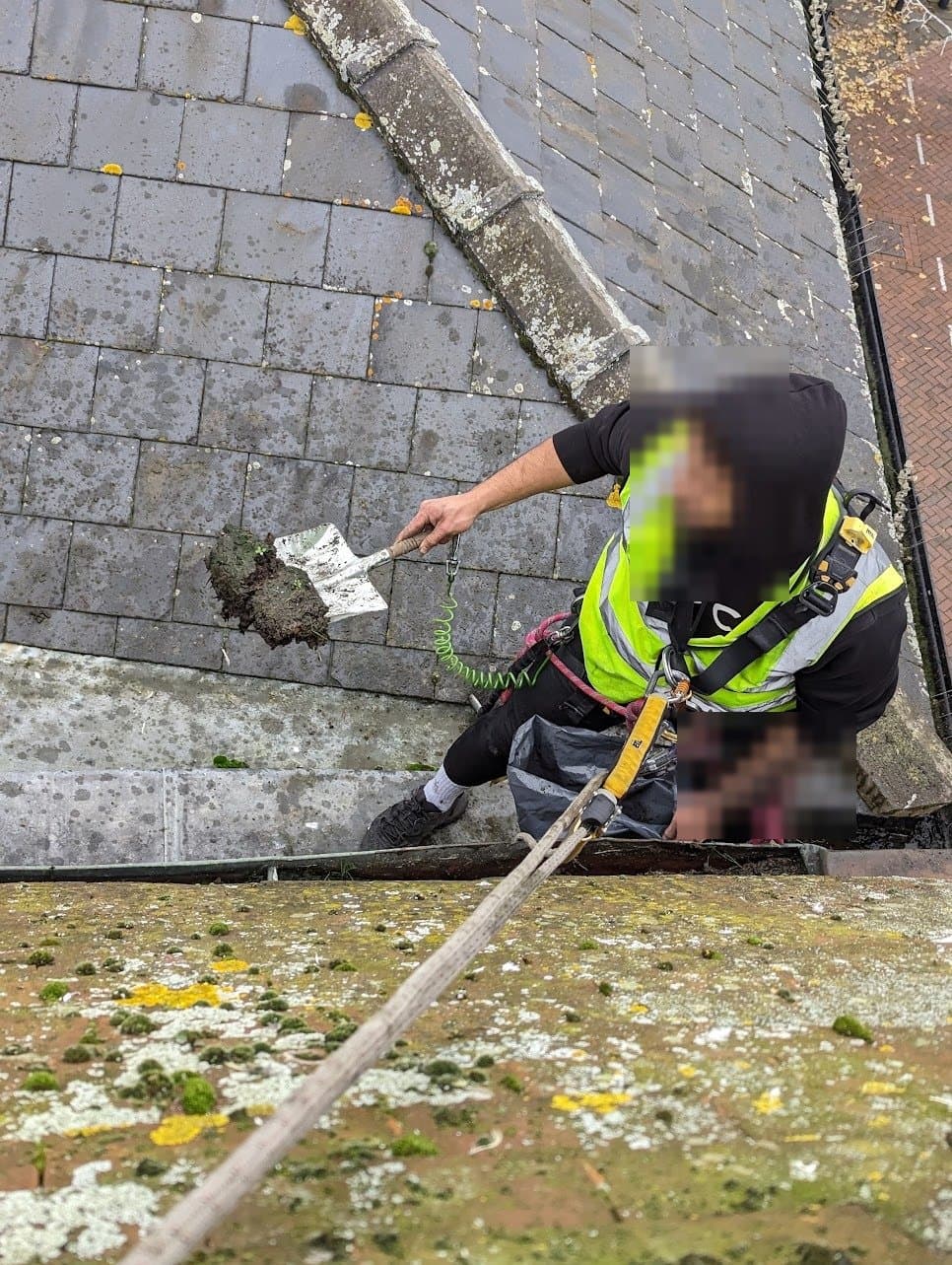 IRATA technician on ropes with harness and back-up device clearing the parapet gutter by shovel