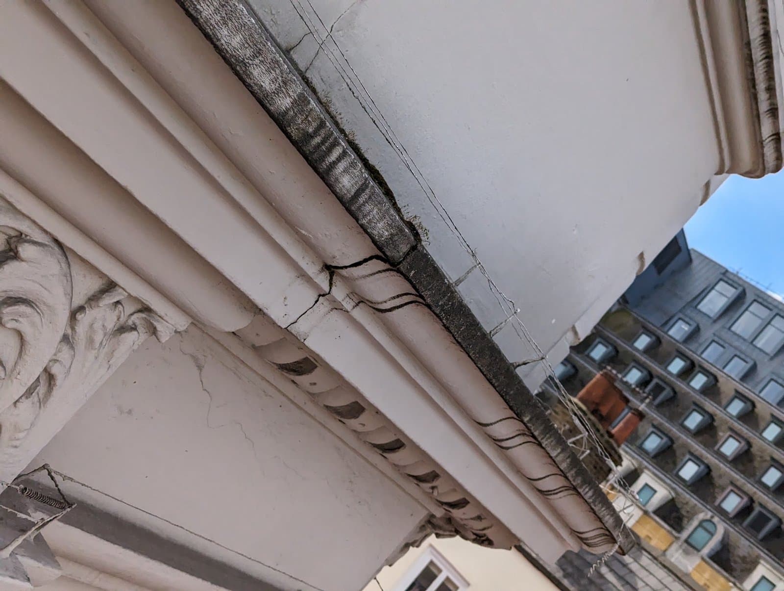 Before: cracked, soot-blackened stucco cornice with anti-pigeon wires across the moulding